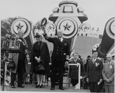 Photograph of Admiral Chester Nimitz on speaker's platform in front of battleship mock-up, waving his hat to the crowd. - NARA - 199215
