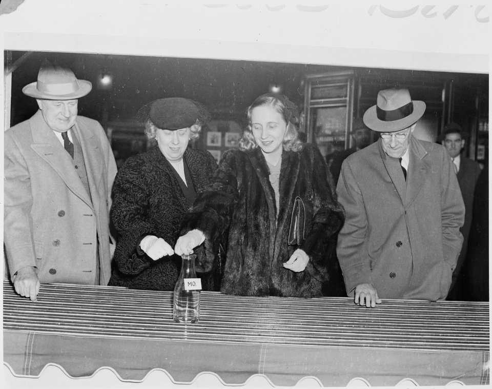 Photograph of Bess Truman and Margaret Truman preparing to drop coins in a bottle marked Mo. as part of a public... - NARA - 199309