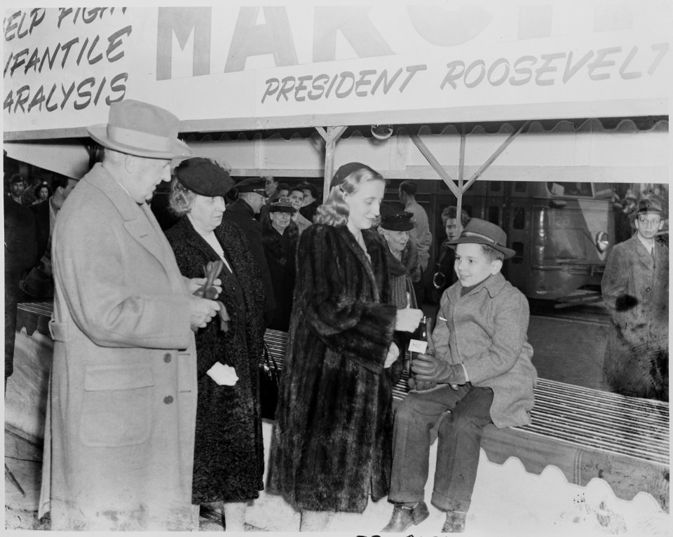 Photograph of Margaret Truman dropping a coin in a bottle held by a young boy as part of a public appearance in... - NARA - 199306