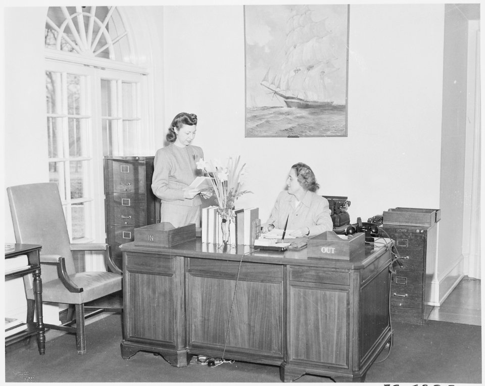 Photograph of President Truman's secretary, Rose Conway, at her desk in the White House, conversing with an... - NARA - 199488