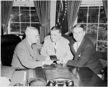 Photograph of President Truman at his desk in the Oval Office, receiving his annual pass to National Football League... - NARA - 200160