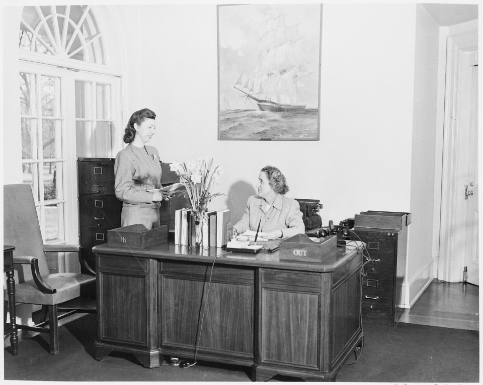 Photograph of President Truman's secretary, Rose Conway, at her desk in her White House office, conversing with an... - NARA - 199484