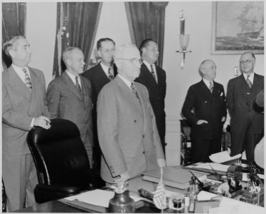 Photograph of President Truman standing at his desk in the Oval Office, with members of his Cabinet standing nearby... - NARA - 199517 photo