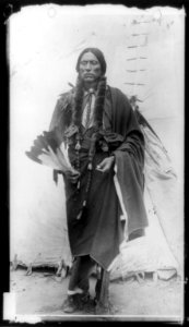 Quanah Parker, Comanche Indian Chief, full-length portrait, standing, facing front, holding feathers, in front of tepee LCCN89714963 photo