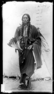 Quanah Parker, Comanche Indian Chief, full-length portrait, standing, facing front, holding feathers, in front of tepee LCCN89714963