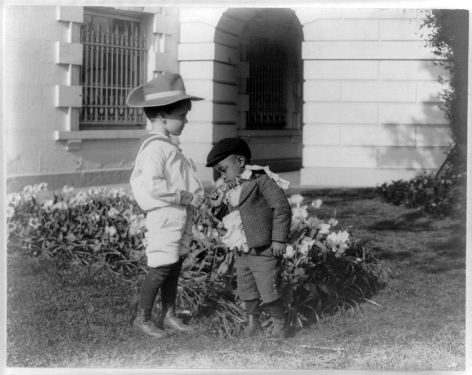 Quentin Roosevelt as a child in front of a flower garden and Roswell Newcomb Pinckney smelling a flower at the White House, Washington, D.C. LCCN2001704016
