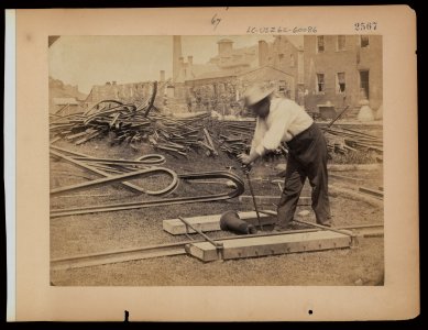 Railroad construction worker straightening track; pile of twisted rails in background. 1862-63 LCCN2005679906