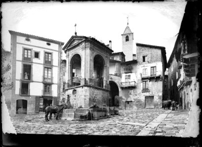 Plaça Sant Joan de Solsona amb un cavall bevent aigua en una font i una església al fons