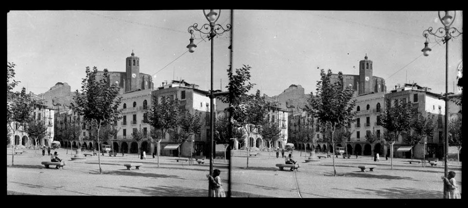 Plaça Mercadal de Balaguer amb arbres, pòrtics i l'església que sobresurt darrera les cases