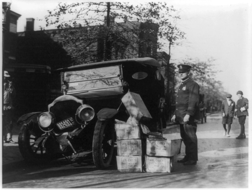 Policeman standing alongside wrecked car and cases of moonshine LCCN89709481