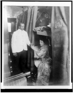 Porter handing young woman a glass of water in railroad sleeping car LCCN96510256