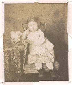 Portrait of an unidentified girl, full-length studio portrait, facing front, seated with right elbow resting on a table and with her left hand on the edge of the table, next to a dog LCCN2015651561