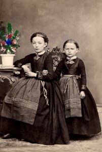 Porträtt av två flickor i klänningar och randiga förkläden. Bara hd. Skåne - Nordiska Museet - NMA.0039734