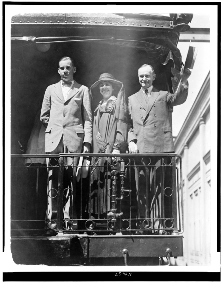President Calvin Coolidge, full-length portrait, standing, facing slightly left, with wife and son, on back of railroad train LCCN95504445