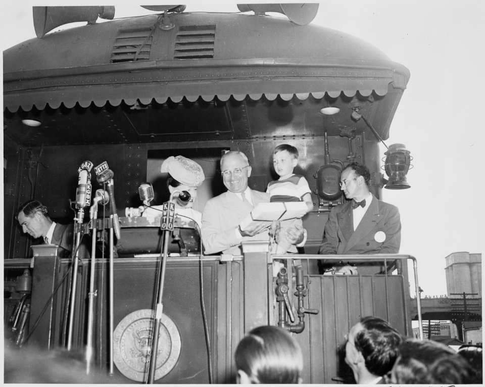 President Harry S. Truman standing on the rear platform of the presidential train, holding a small boy and a present.... - NARA - 199927