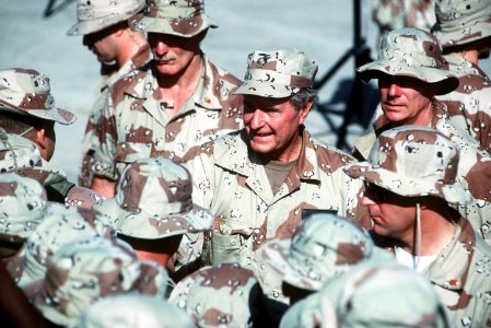 President George H. W. Bush shakes hands and speaks to individuals as he walks through a crowd of U.S. troops at the airport