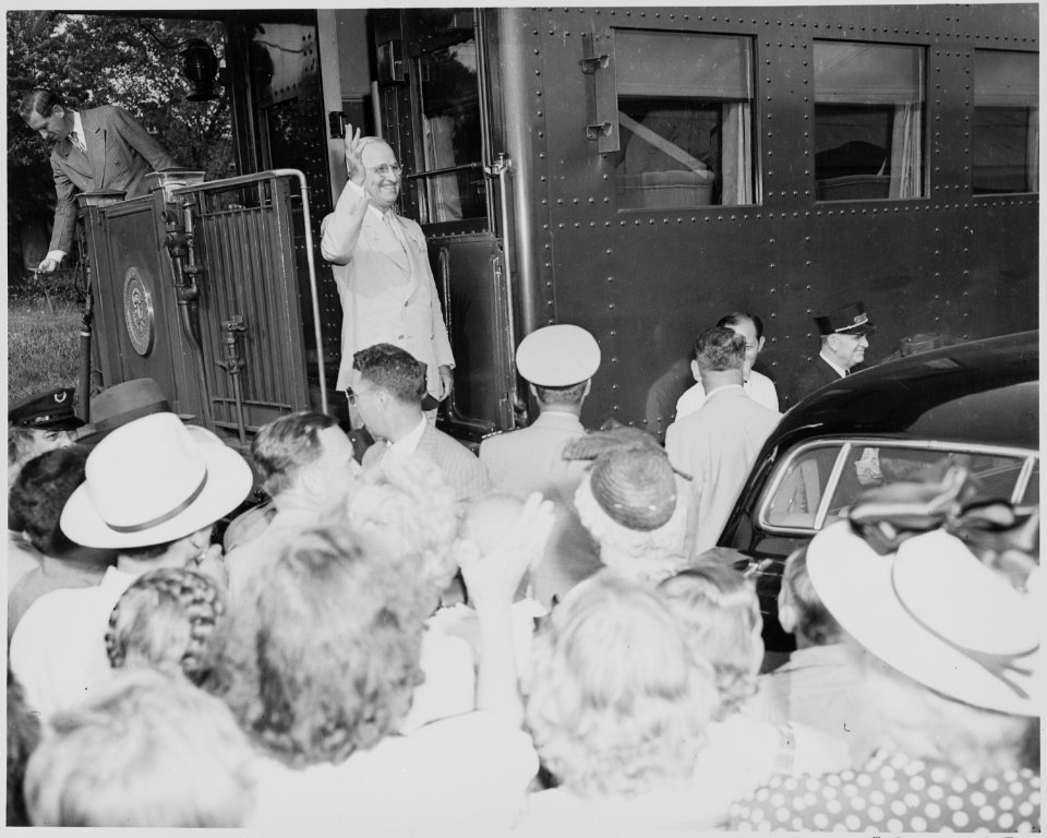 President Harry S. Truman standing on the lower step of the rear platform of the presidential train, waving to the... - NARA - 199926