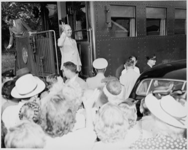 President Harry S. Truman standing on the lower step of the rear platform of the presidential train, waving to the... - NARA - 199926