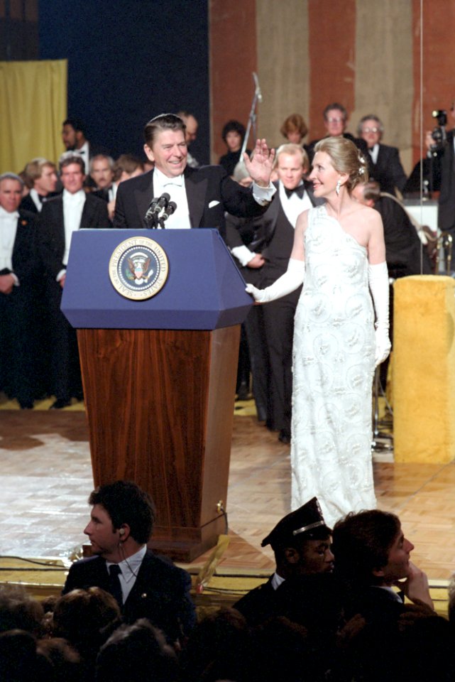 President Ronald Reagan and Nancy Reagan standing behind podium waving at Inaugural Ball at American History Museum