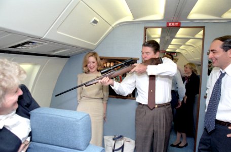President Ronald Reagan pointing a rifle out a window while flying aboard Air Force One during trip to California photo
