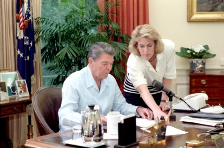 President Ronald Reagan sitting at his desk prior to his radio address to the Nation on International Trade in the Oval Office with Caroline Rhoden