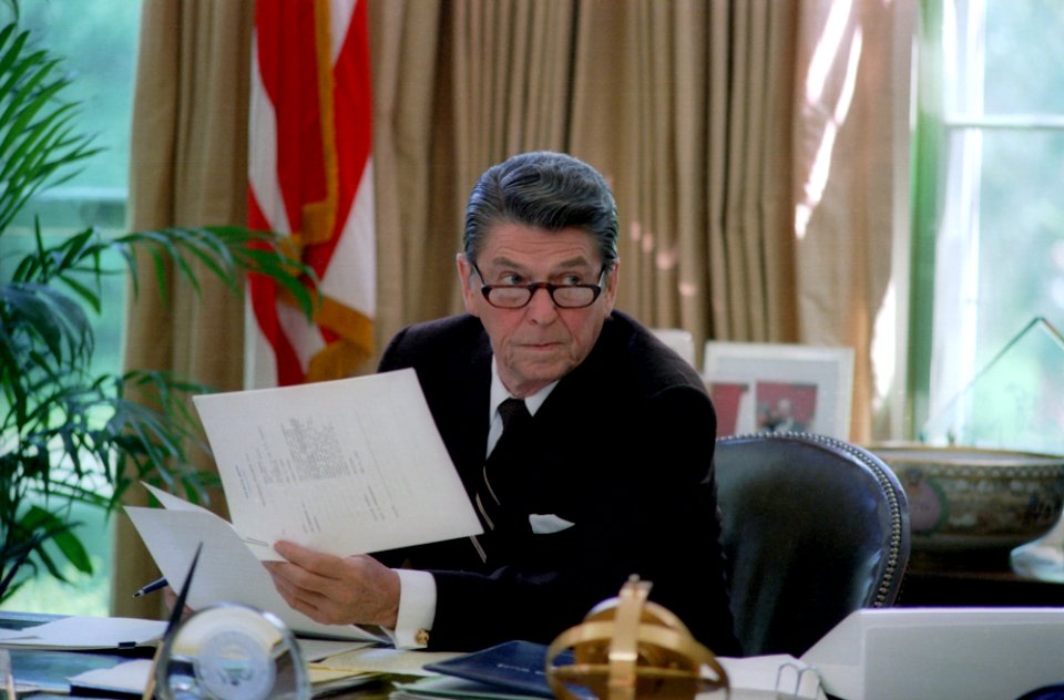 President Ronald Reagan wearing glasses while working at his desk in the oval office