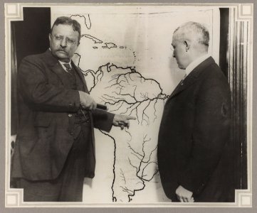 President Roosevelt pointing at a map of South America towards the area explored during the Roosevelt-Rondon Scientific Expedition in Brazil as another man looks on LCCN2009633768