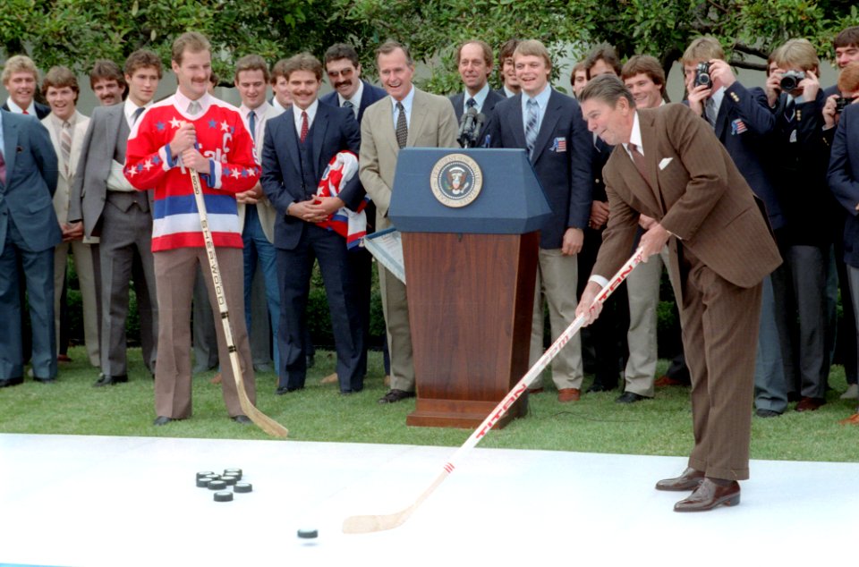 President Ronald Reagan hitting a hockey puck during a White House event for the United States Olympic hockey team and Washington Capitals hockey team in the Rose Garden