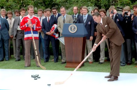 President Ronald Reagan hitting a hockey puck during a White House event for the United States Olympic hockey team and Washington Capitals hockey team in the Rose Garden