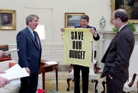 President Ronald Reagan holding up a T shirt with Larry Speakes and Dennis Thomas in the Oval Office