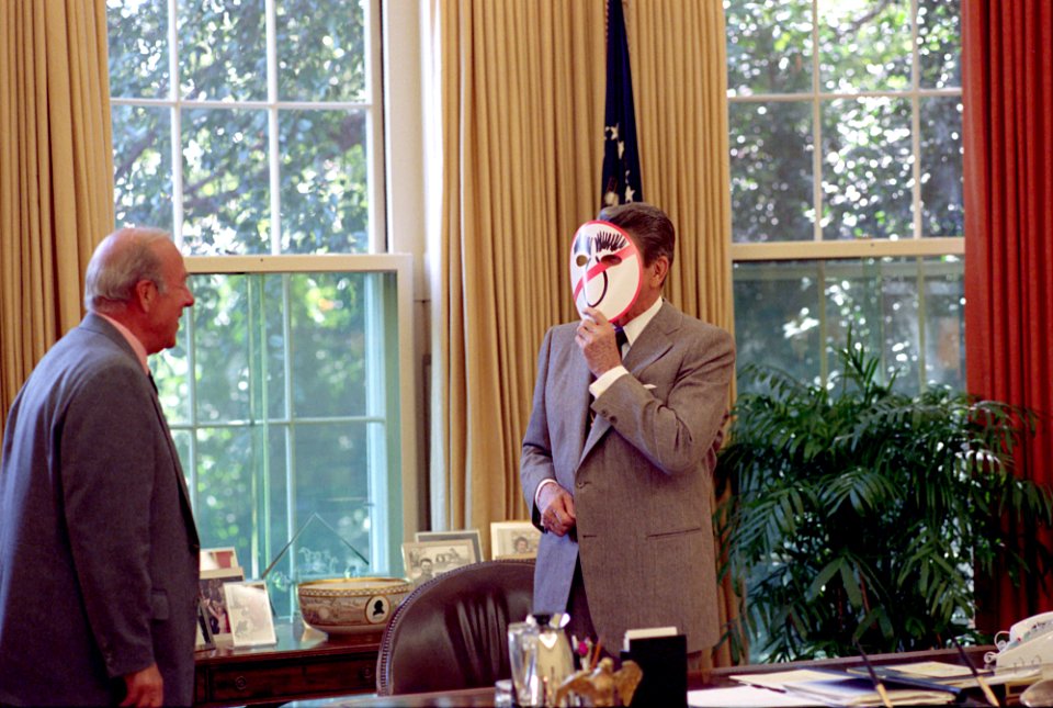 President Ronald Reagan wearing an Anti-Dukakis mask and showing George ShultZ in the Oval Office