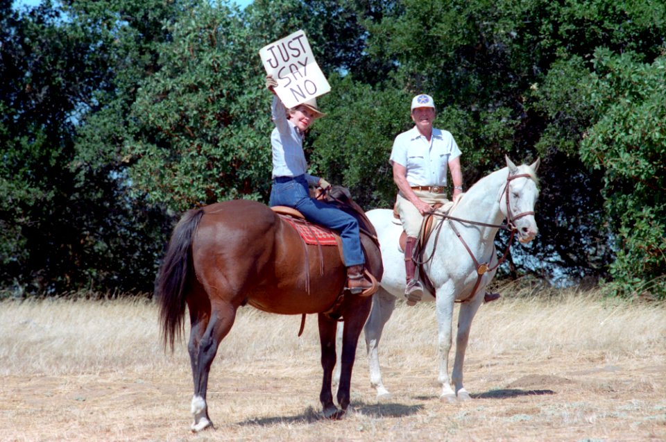 President Ronald Reagan with Nancy Reagan who holds up a Just Say No sign for press photographers while riding horses at Rancho Del Cielo