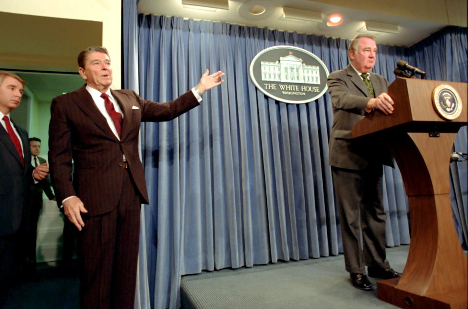 President Ronald Reagan motioning to Ed Meese after making an announcement to the press regarding the National Security Council and the implementation of United States Policy towards Iran in press room