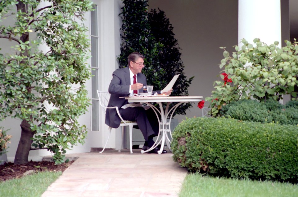 President Ronald Reagan reading with glasses on and eating lunch