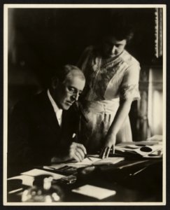 President Woodrow Wilson, seated at desk with his wife, Edith Bolling Galt, standing at his side LCCN2005684886