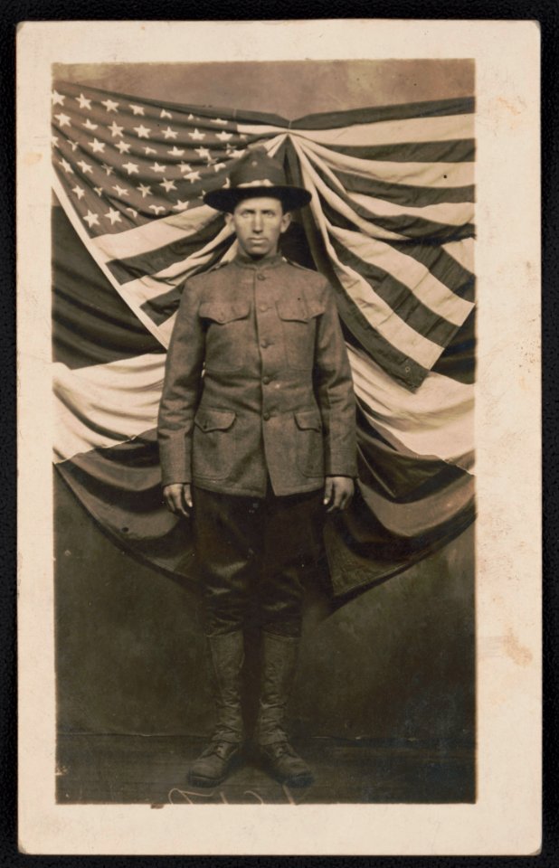 Private John H. Rowe of Co. B, 16th Infantry Regiment in uniform in front of flags LCCN2018645953