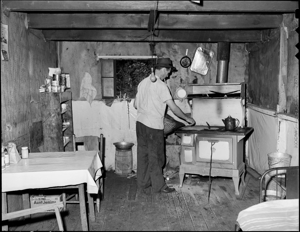 Ray Boggess, a miner, building a fire in his home in company housing project. This one room, converted garage, rents... - NARA - 540945