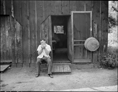 Ray Boggess, miner, sitting in front of the converted garage, in company housing project, which serves him as a... - NARA - 540943
