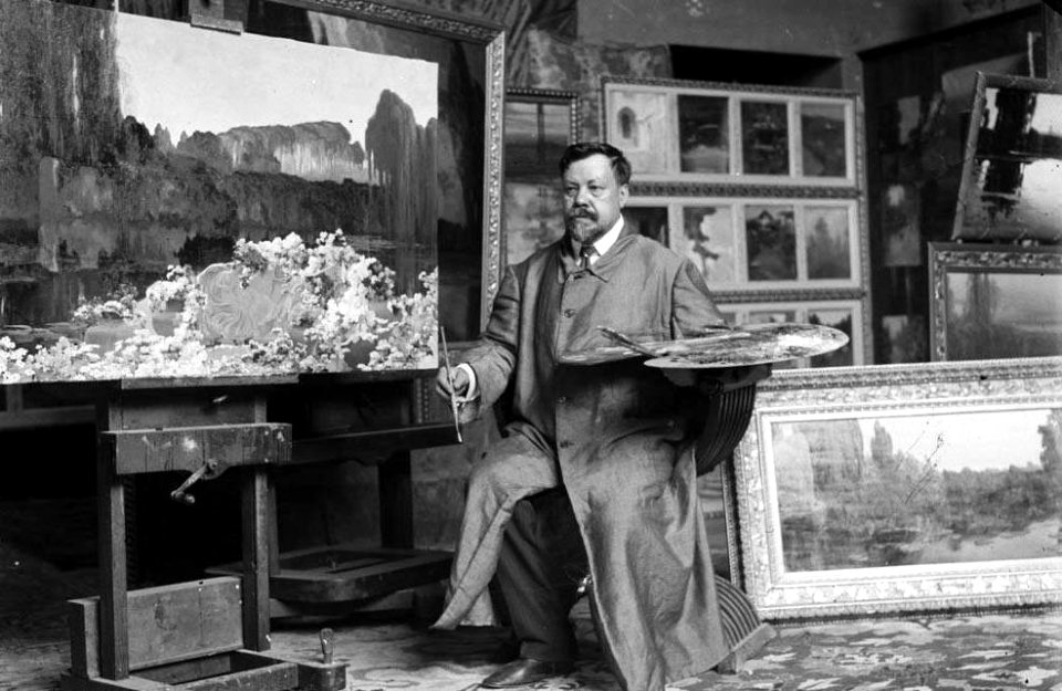 Retrat del pintor Enric Serra Auqué al seu estudi voltat de quadres (cropped)