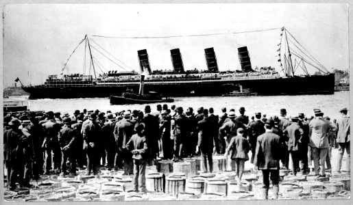RMS Lusitania, New York City, September 1907, stern-side view, during maiden voyage, with a large crowd of men, in foreground, standing on top of barrels LCCN2002721375
