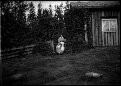 Rökstugubyggnad. Kvarntorp. Detaljbild exteriört rökstugan med kvinna med barn i kolt - Nordiska museet - NMA.0091168 photo
