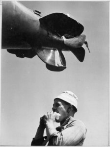 Sailor eating sandwich beneath propellers of torpedo being loaded aboard U.S. submarine at New London, Connecticut. - NARA - 520850