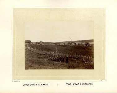 Samisk gårdstun med skigard rundt. Noen samer sitter i forgrunnen ved treskjelettet til en gamme - Norsk folkemuseum - NF.15006-029