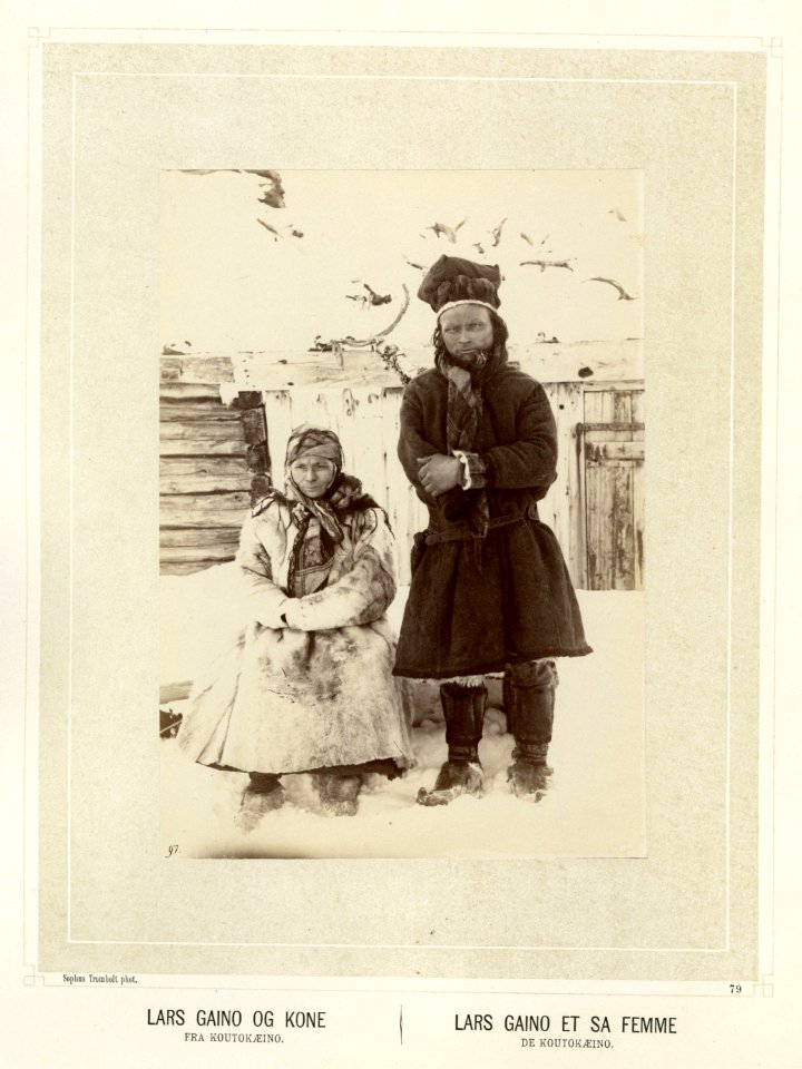Samen Lars Gaino og hans kone i pesk, sjal og skaller. Oppstilt foran tømmerbygning - Norsk folkemuseum - NF.15006-081