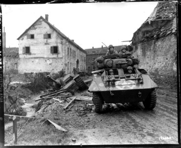 SC 196666 - An M8 reconnaissance armored car of the 30th Infantry Div., rolls through the streets of Kinzweiler, November 21, 1944
