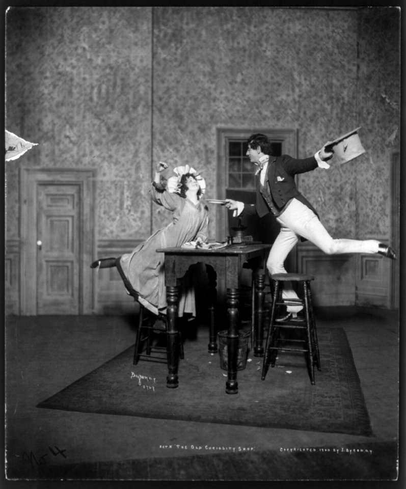 Scene from Act II of The Old Curiosity Shop, showing young man and girl dancing on office stools around table LCCN2004681925