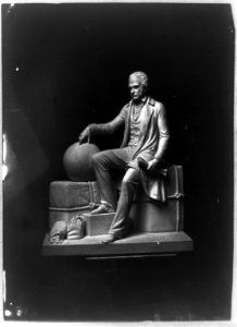 Sculpture of sitting man with his hand on globe and sacks of money at his feet LCCN2002717764