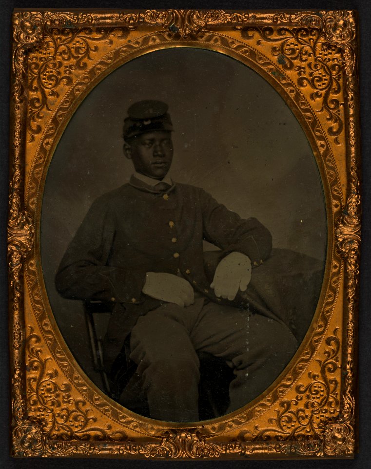 Seated black soldier, frock coat, gloves, kepi LCCN2002719395