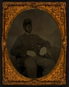 Seated black soldier, frock coat, gloves, kepi LCCN2002719395