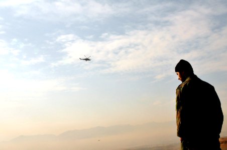 An Afghan National Army soldier stands overlooking the valley on the outskirts of the city of Kabul as a soviet HIND MI35 attack helicopter patrols the area (4335158866)